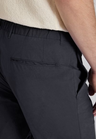 Black pants feature a smooth texture, elastic waistband, and side pockets. They include a sleek design with minimal stitching and a single rear pocket.