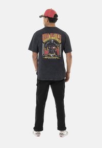 T-shirt graphique noir avec un design de moto, du texte et des accents à carreaux au dos. Associé à un pantalon noir et des chaussures à carreaux.