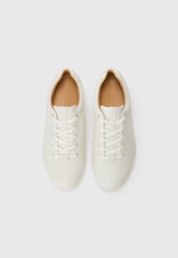 Une paire de baskets blanches en cuir, à lacets, avec des semelles intérieures rembourrées en tan, vue de dessus sur un fond blanc.