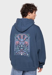 Sudadera azul marino con un gran estampado gráfico en la parte posterior, que presenta diseños abstractos coloridos, llamas y formas geométricas. Material de algodón.