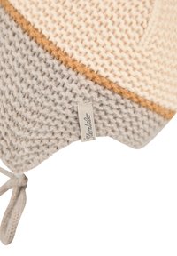 Strickmütze in einer Mischung aus Creme-, Grau- und Brauntönen, mit einem strukturierten Muster und Kordelzügen, mit einem Etikett an der Seite.