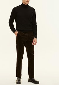 Maglione collo alto nero abbinato a pantaloni di velluto a coste marroni scuri e scarpe eleganti nere. Texture lisce, design aderente e silhouette su misura.
