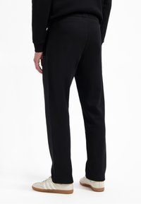 Schwarze Sweatpants aus weichem Stoff mit einem elastischen Bund und tapered Beinen. Getragen mit hellen Turnschuhen.