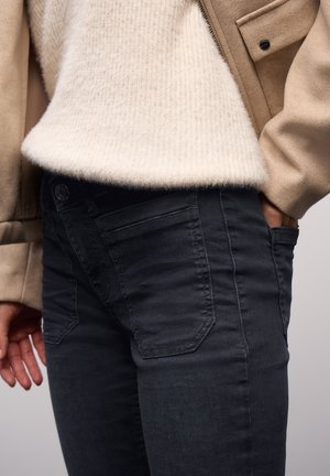 Zwarte jeans met een aansluitend ontwerp, voorzien van voorzakken en een gestructureerde stof. Draag ze met een licht, pluizig crèmekleurig truitje.