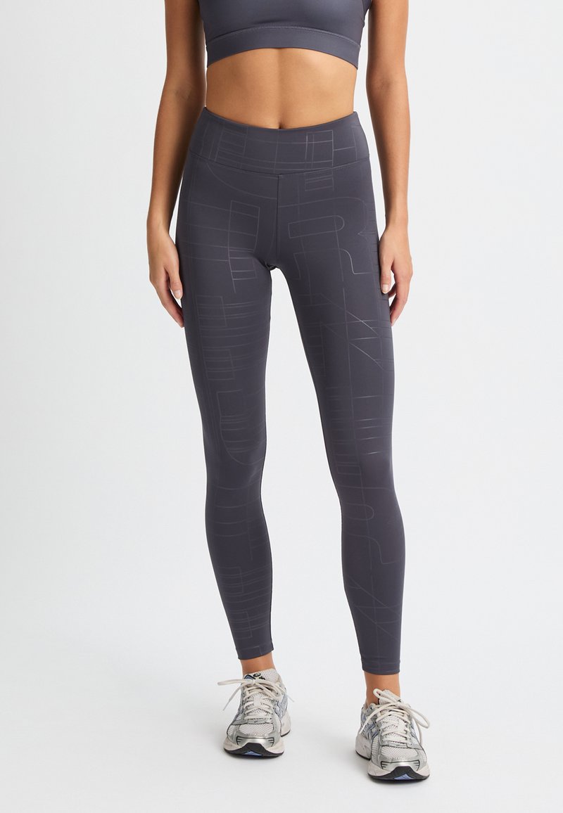 Leggings de tiro alto en gris oscuro con un sutil patrón geométrico, fabricados en tela elástica. Presentan una cinturilla suave y un diseño hasta el tobillo.