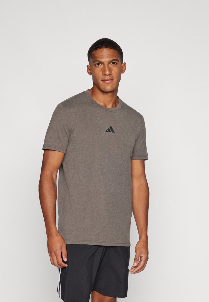 Salātu zaļš t-krekls ar īsām piedurknēm un apaļu kaklu, ar melnu Adidas logo uz krūtīm. Audums izskatas mīksts un viegls.
