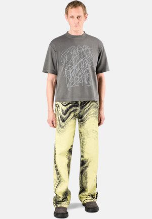 Gray cotton t-shirt with blue abstract design, paired with yellow denim pants featuring a black swirl pattern and black footwear.