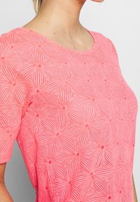Top rosa de manga corta con un patrón texturizado de líneas entrelazadas que forman formas de flores, con un escote redondo.