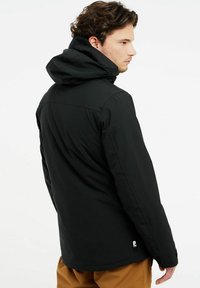 Schwarze isolierte Jacke mit Kapuze, die ein elegantes Design, strukturierten Stoff und ein Markenakzent auf dem unteren Rücken aufweist.
