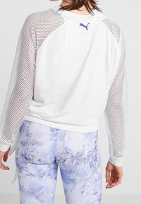 Donna che indossa una felpa Puma con maniche in rete bianca e leggings leggeri con motivo marmorizzato blu chiaro, mostrata di spalle.