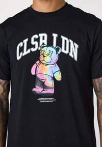 Sort bomulds T-shirt med et farverigt tegnefilmsbjørn grafik med krydsede øjne, og fede bogstaver "CLSR LDN" trykt ovenfor.