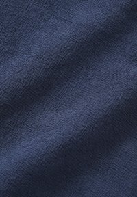 Gros plan d'un tissu texturé bleu foncé avec un motif tissé subtil et des plis doux créant des ombres douces.
