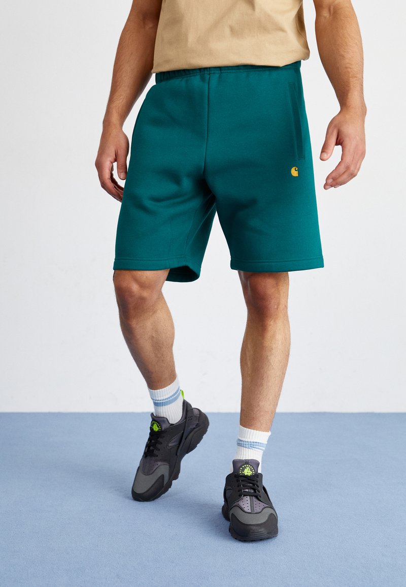 Türkise Shorts aus weichem Stoff, mit einem elastischen Bund und seitlichen Taschen, kombiniert mit schwarzen Sneakers und hellblau gestreiften Socken.