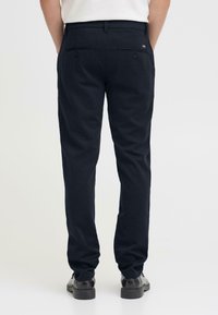 Pantaloni blu navy in cotone con taglio dritto, dotati di due tasche posteriori con bottoni e passanti per cintura, abbinati a scarpe nere.