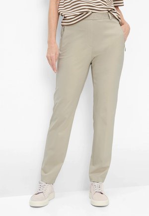 Kvinde iført beige bukser med lige ben og lynlåslommer i siden, en kortærmet top med striber og lyserøde snørestøvler.