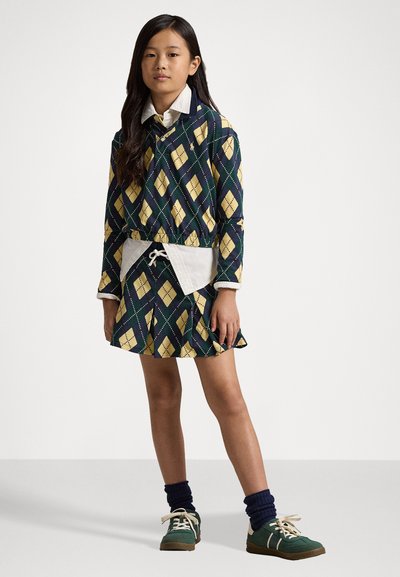 A színes ruha gyémánt mintázattal készült sötétkéken, sárgában és zöldben; fehér inggallérral és zsinóros derékkal rendelkezik. Zöld cipővel viselik.