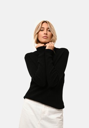 Maglione nero a coste con alto collo e maniche lunghe. La vestibilità è morbida e rilassata, abbinato a un capo inferiore di colore chiaro.