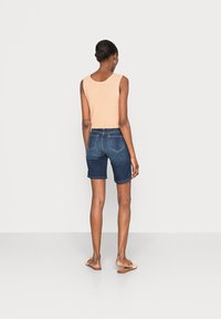 Top sin mangas beige combinado con shorts de mezclilla azul medio. Los shorts tienen bolsillos traseros y un corte recto, acompañados de chanclas.