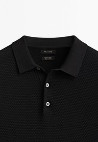 Polo noir en tissu tricoté texturé, doté d'un col, d'une fermeture à trois boutons et d'une étiquette avec les détails de la marque.