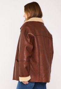 Veste en cuir marron avec col et poignets en peau lainée. Design surdimensionné, avec poches latérales et détails cousus dans le dos.