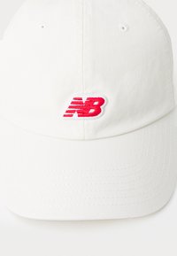 Cască de baseball albă din bumbac, cu un logo roșu „NB” brodat pe față. Prezintă o visieră curbată și un material texturat.