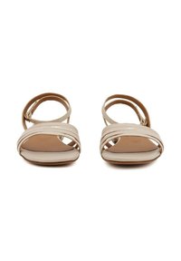 Sandali beige con punta aperta e suola piatta, caratterizzati da cinturini intrecciati e una cinghia alla caviglia regolabile. Materiale liscio con un design minimalista.