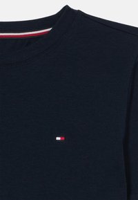 Μπλε ναυτικού χρώματος μπλουζάκι με στρογγυλή λαιμόκοψη και μικρό ορθογώνιο λογότυπο σε κόκκινο, λευκό και μπλε στο αριστερό στήθος και ριγωτή λεπτομέρεια στο εσωτερικό γιακά.