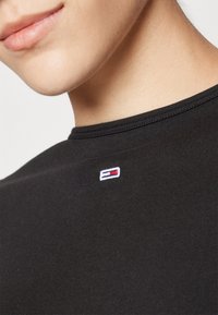 T-shirt in cotone nero con scollatura rotonda. Presenta un piccolo logo ricamato con accenti rossi, bianchi e blu nella zona sinistra del petto.