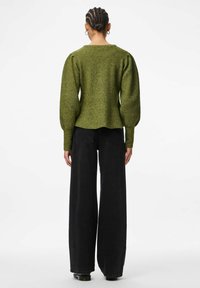 Zielono-oliwkowy sweter z dzianiny z bufkami na rękawach, prążkowaną fakturą i falbaniastym dołem, w połączeniu z ciemnymi dżinsami o wysokim stanie.