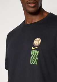 Sort bomulds T-shirt med et tegneserie-basketball grafik og grønt netdesign. Inkluderer et lille gult Nike-logo over grafikken.