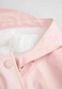 Jasnoróżowy płaszcz przeciwdeszczowy z miękką białą podszewką z sztucznego futra. Wyposażony w zaokrąglony kołnierz i zapięcie na zatrzask z przodu. Gładki, wodoodporny materiał.