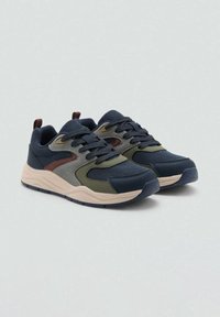 Par čevelj zavezovanje v temno modri in olivno zeleni barvi z bež podplati na svetlo sivi podlagi.