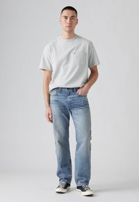 Grijze korte mouwen t-shirt met een zak, gecombineerd met lichtblauwe rechte spijkerbroek en zwarte sneakers met witte details.