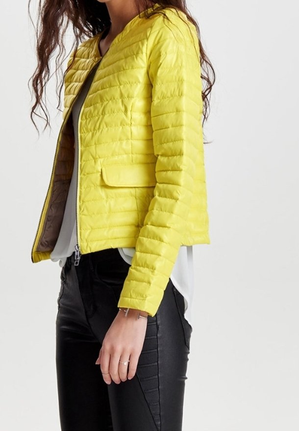 Yellow quilted bomber jacket with a rounded neckline, zip closure, and side pockets; worn over a layered gray top and black pants.