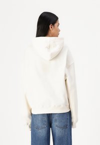 Light cream hoodie with a drawstring hood, oversized relaxed fit, and ribbed cuffs, paired with high-waisted blue denim jeans.