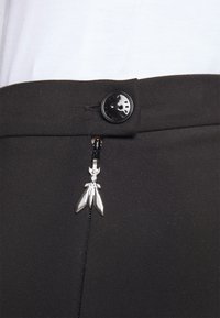 Schwarze, maßgeschneiderte Hose mit glatter Textur, einem Knopfverschluss und einem dekorativen silbernen Reißverschluss, der einem Insekt ähnelt.