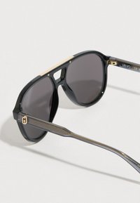 Fekete napszemüveg szürke lencsékkel, arany díszítéssel a tetején, és mintás ezüst szárakkal. Simított műanyag keret és elegáns, modern kialakítás.