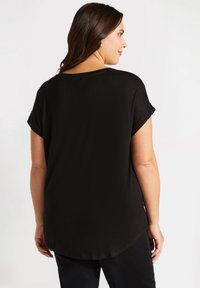 Svart kortärmad topp med rundad halsringning och längre bakre nederkant, tillverkad av mjukt tyg med en slät textur. Inga märkbara mönster eller detaljer.