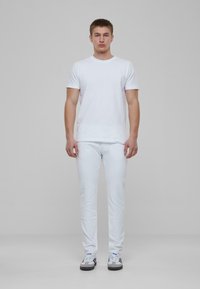 Camiseta blanca de cuello redondo, jeans blancos desgastados y zapatillas deportivas grises con acentos azules. Diseño simple y minimalista.