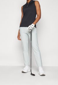 Černé bezrukávové polo tričko se třemi knoflíky, světle modré golfové kalhoty, bílé golfové boty a bílá rukavice držící golfovou hůl.