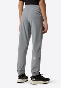 Grå treningsbukser med elastisk midjebånd, sidelommer og svarte detaljer. Stoffet virker lett og glatt.