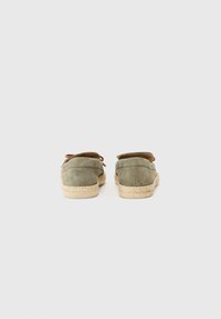 Scarpe slip-on in suede verde con punta arrotondata, suola piatta in juta e dettagli in pelle sul tallone, caratterizzate da una superficie liscia e un design semplice.