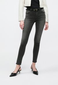 Γκρίζα στενά τζιν με μεσαία μέση, πέντε τσέπες και βρόχους για ζώνη, σε συνδυασμό με μαύρες γόβες slingback με λεπτομέρεια φιόγκου.