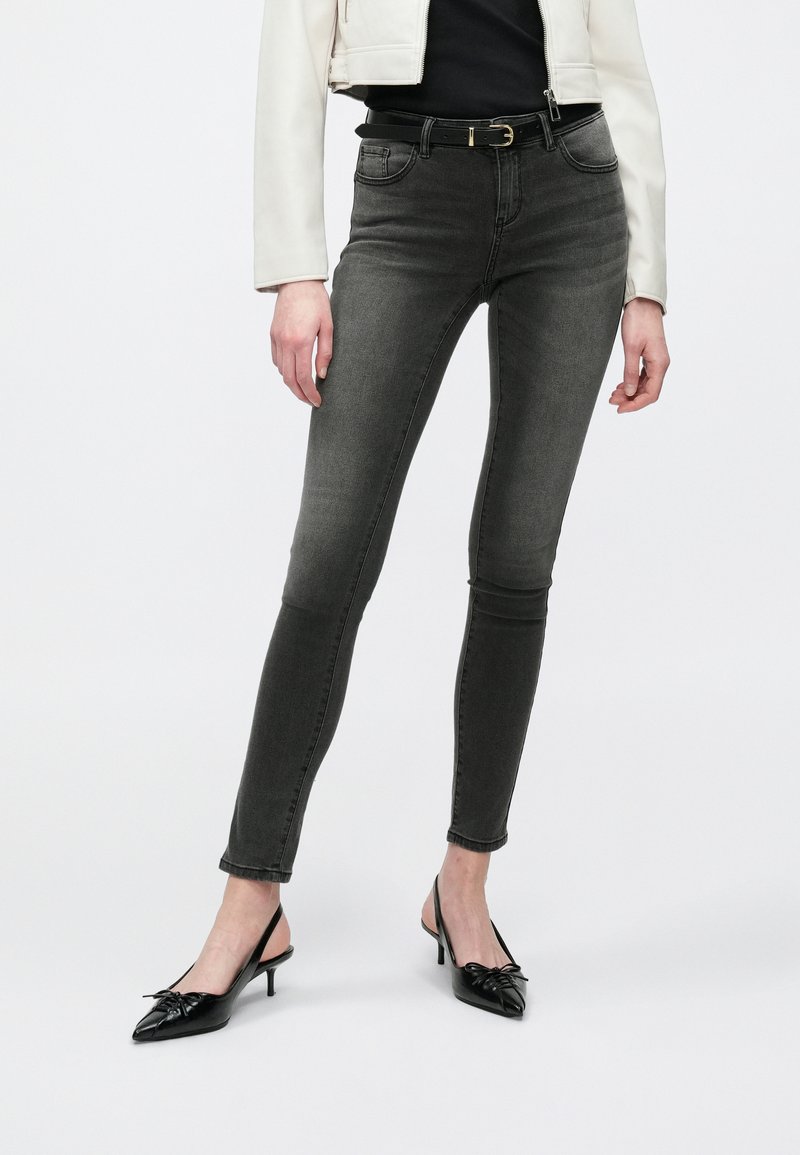 Γκρίζα στενά τζιν με μεσαία μέση, πέντε τσέπες και βρόχους για ζώνη, σε συνδυασμό με μαύρες γόβες slingback με λεπτομέρεια φιόγκου.