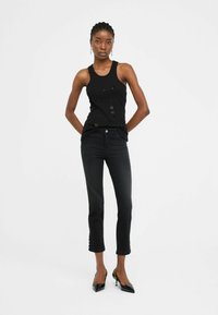 Débardeur noir avec des ornements, associé à un jean noir ajusté avec des détails sur les côtés et complété par des escarpins noirs à bout pointu.
