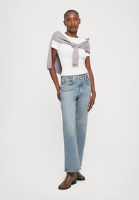 White fitted t-shirt, light blue straight-legged jeans, light lavender knit sweater draped over shoulders, and brown ankle boots.