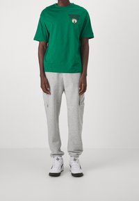 Grön bomull t-shirt med "BOSTON CELTICS" logotyp, parat med grå fleece sweatpants med fickor och elastiska muddar, bärs med vita sneakers.