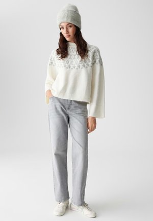 White knit sweater with gray pattern at the top, paired with light gray straight-leg jeans and white sneakers. Model wearing a matching gray beanie.