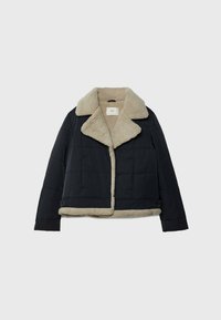 Sort quilted jakke med beige faux shearling-fór, bred krave og manchetter, liggende fladt på en ensfarvet baggrund.