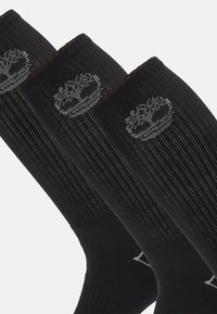 Calzini neri con un design a coste, caratterizzati da un logo di un albero grigio vicino al polsino. Presentano una texture liscia e una lunghezza alla caviglia.